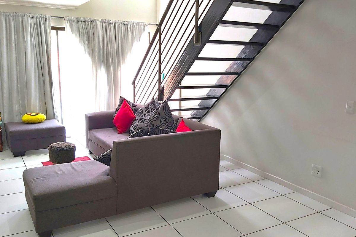 A living room featuring tiled flooring and an open-tread staircase with a metal balustrade, leading to an upper level with access to a patio.