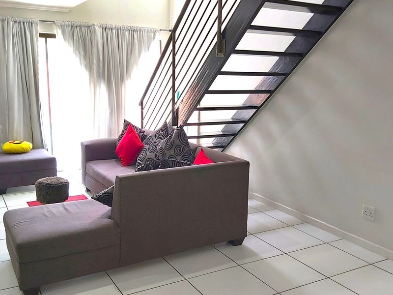 A living room featuring tiled flooring and an open-tread staircase with a metal balustrade, leading to an upper level with access to a patio.