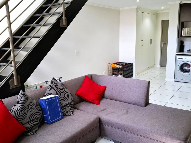 Open-plan living area featuring a modern staircase, tiled flooring, and a compact kitchen with built-in cabinetry and integrated appliances.