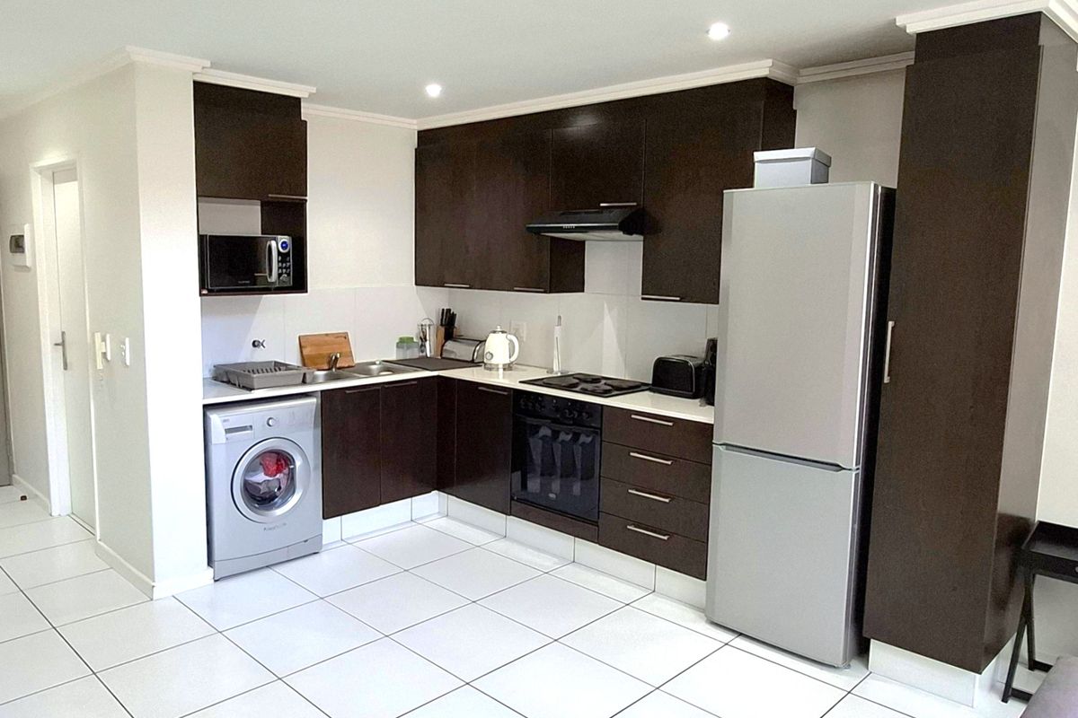 Modern kitchen featuring dark wood cabinetry, integrated appliances, stainless steel sink, and clean tiled flooring with recessed lighting.