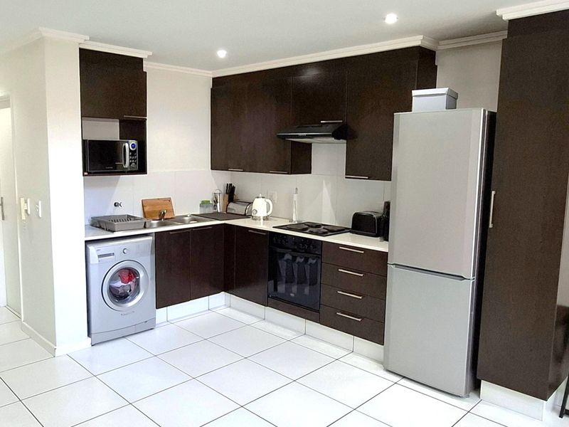 Modern kitchen featuring dark wood cabinetry, integrated appliances, stainless steel sink, and clean tiled flooring with recessed lighting.