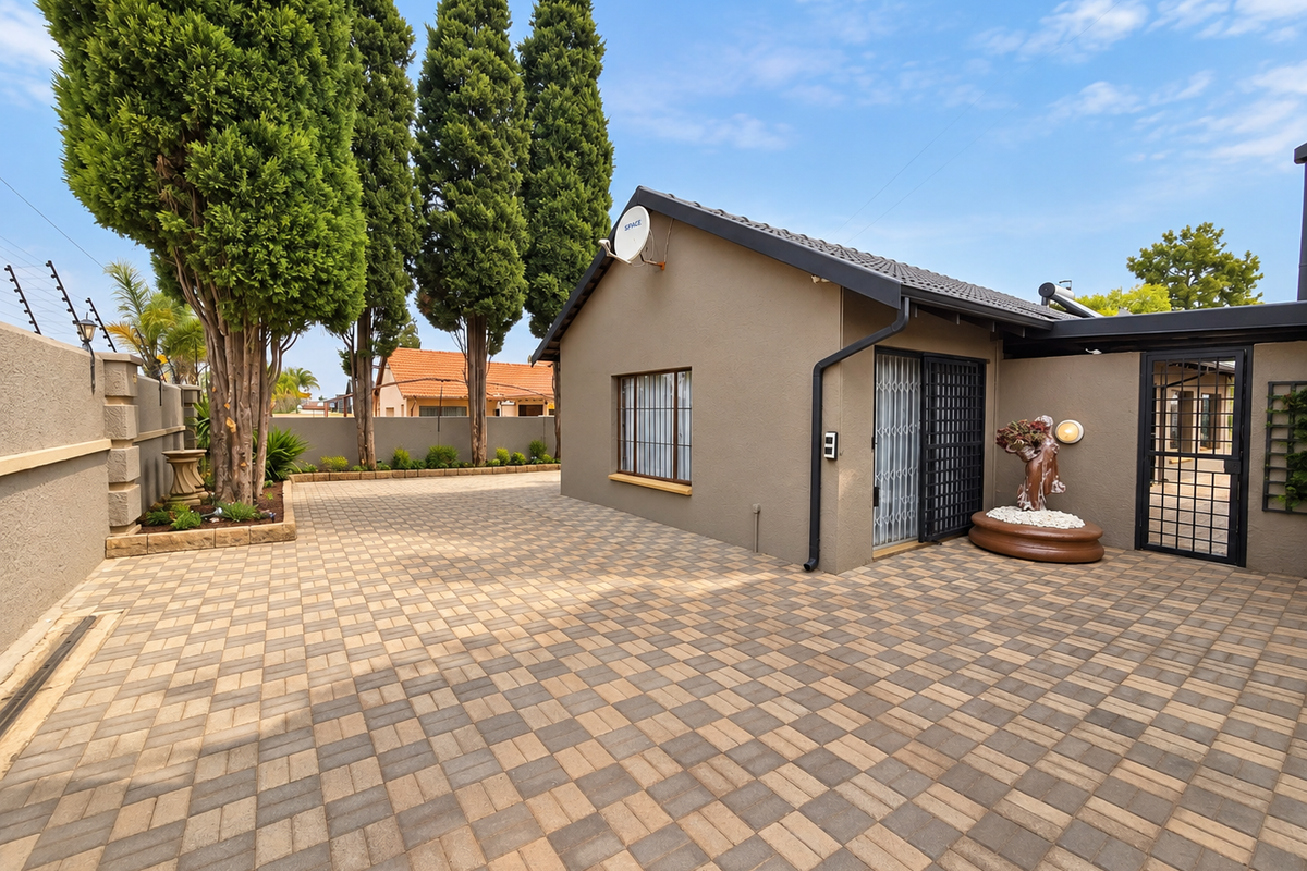 A well-maintained rear exterior area featuring paved surfacing, secure gated access, electric fencing, and established landscaping.