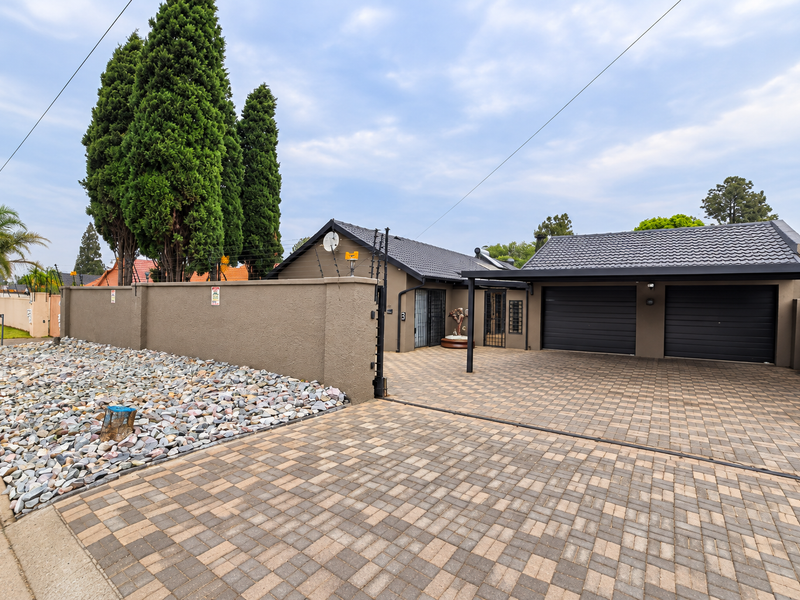 Front view of the property featuring a paved driveway, double garage, and secure perimeter wall with electric fencing.