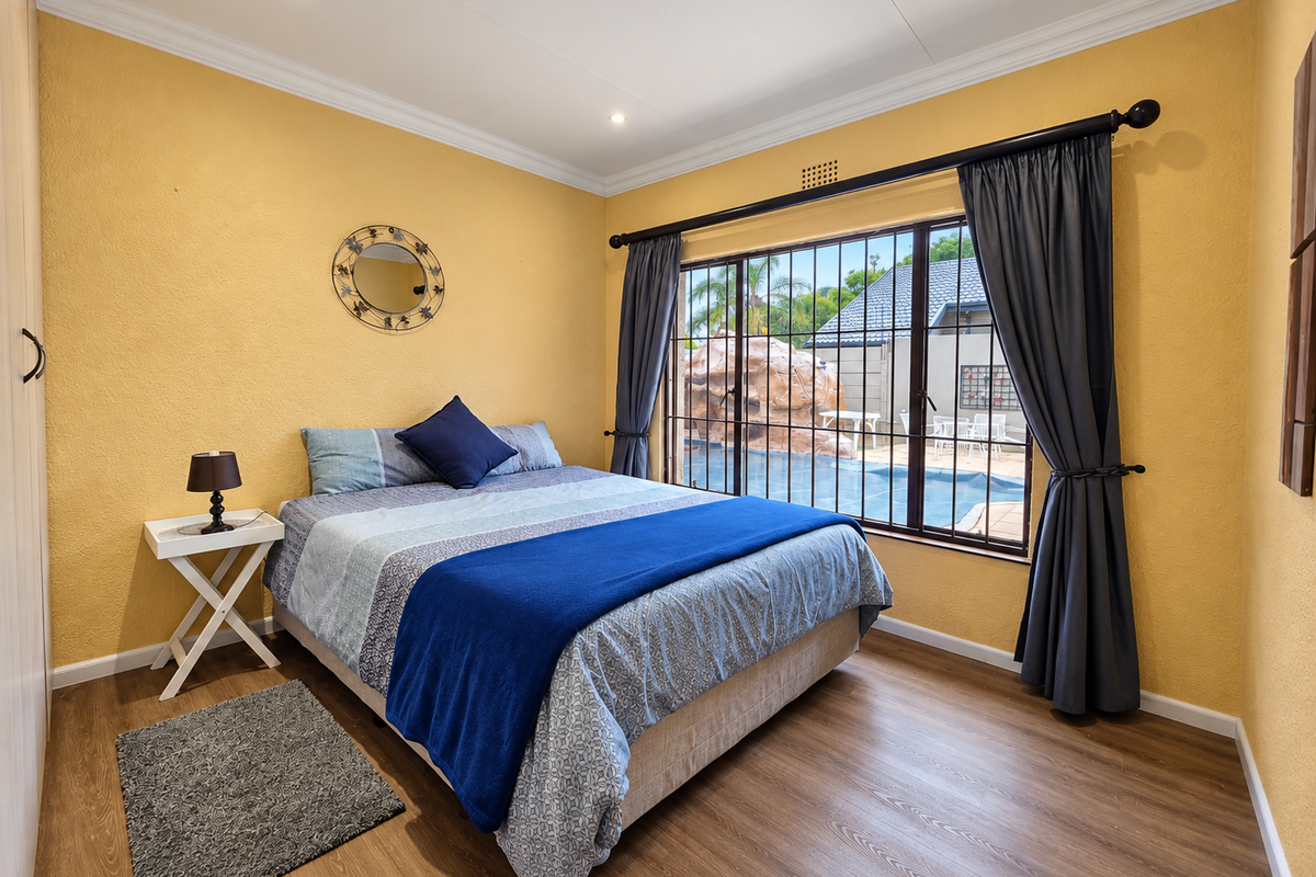 A well-maintained bedroom featuring laminate flooring, recessed lighting, and a built-in wardrobe, with direct views of the outdoor pool area.