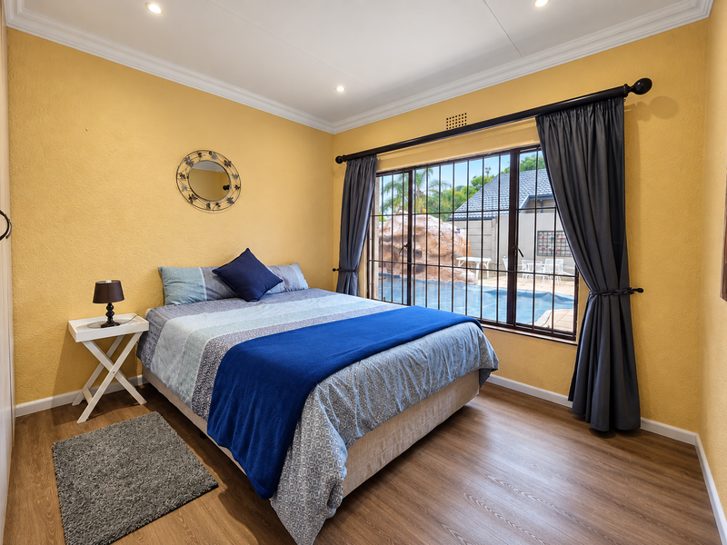 A well-maintained bedroom featuring laminate flooring, recessed lighting, and a built-in wardrobe, with direct views of the outdoor pool area.