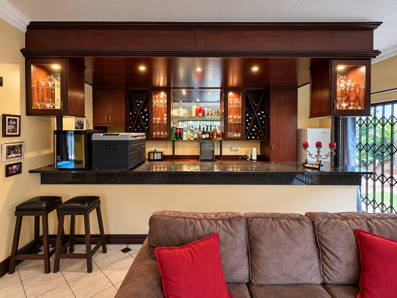 A well-appointed built-in home bar featuring dark wood cabinetry, granite countertops, integrated wine storage, and glass display shelving with recessed lighting.