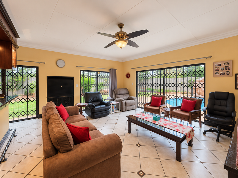 Spacious living room featuring tiled flooring, a ceiling fan, and large sliding glass doors with security gates providing direct access to the pool area.