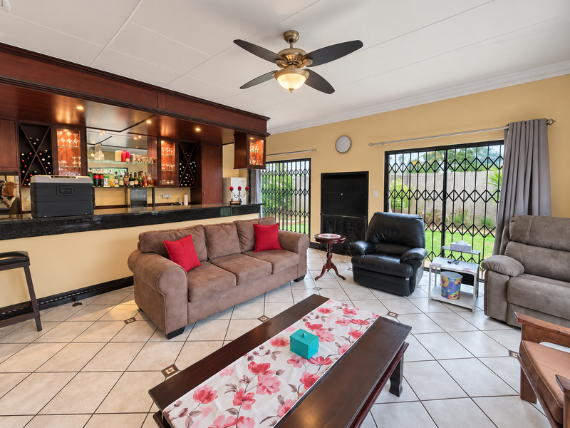 Spacious living area featuring a built-in wooden bar with integrated lighting, tiled flooring, and sliding glass doors leading to the garden.