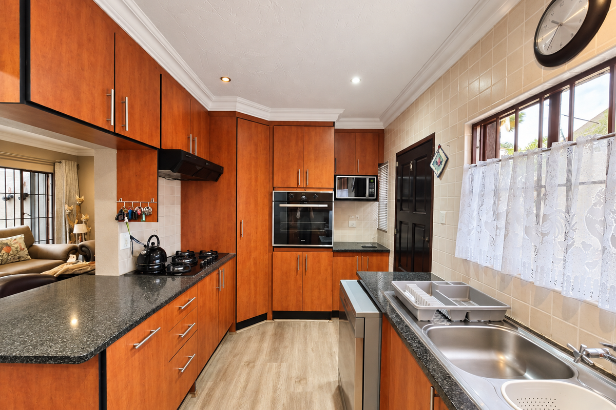 A functional kitchen featuring warm-toned wooden cabinetry, granite countertops, a built-in oven, gas hob, and a double sink with a tiled backsplash.