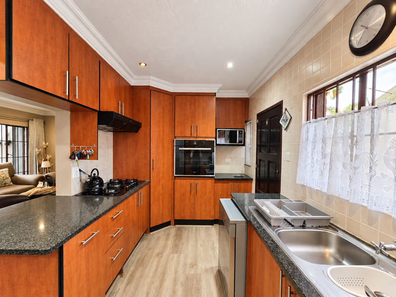 A functional kitchen featuring warm-toned wooden cabinetry, granite countertops, a built-in oven, gas hob, and a double sink with a tiled backsplash.