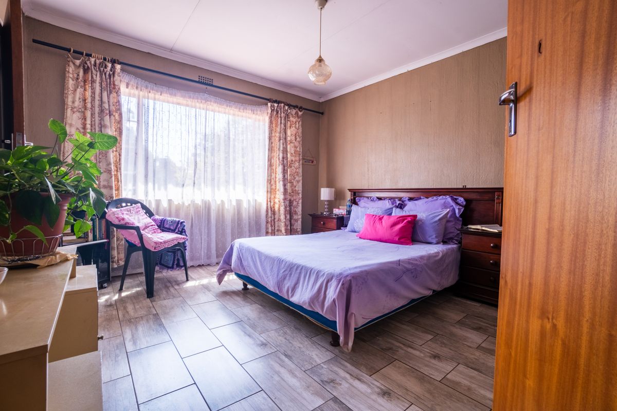 A bedroom featuring tiled flooring, a large window with curtain rods, and a central pendant light fixture.