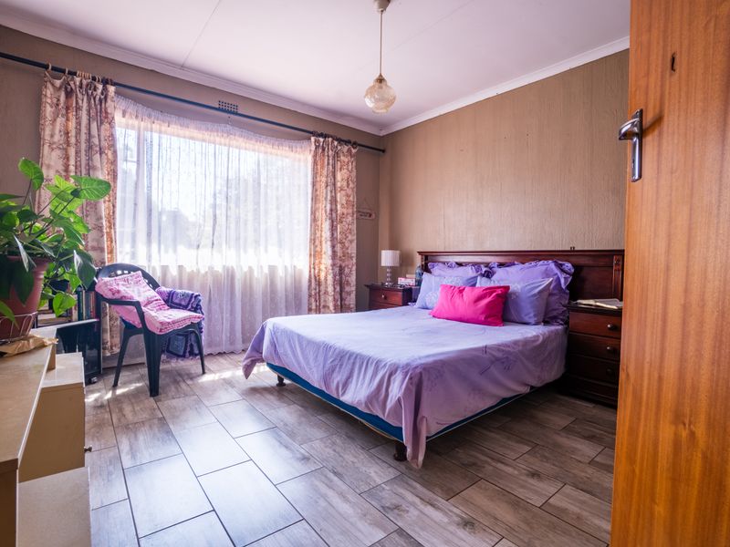 A bedroom featuring tiled flooring, a large window with curtain rods, and a central pendant light fixture.