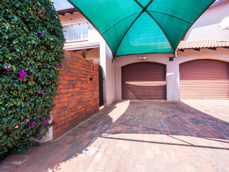 A well-maintained double garage with roller doors, featuring a brick-paved driveway and a protective shade sail structure.