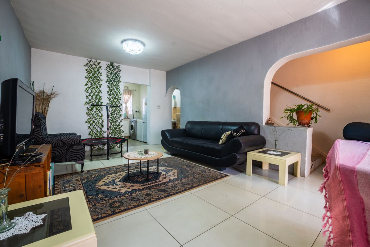 A spacious living room featuring tiled flooring, an arched entryway leading to the staircase, and neutral wall finishes.