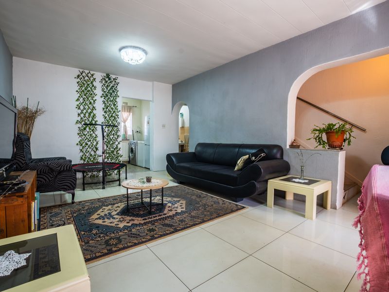 A spacious living room featuring tiled flooring, an arched entryway leading to the staircase, and neutral wall finishes.