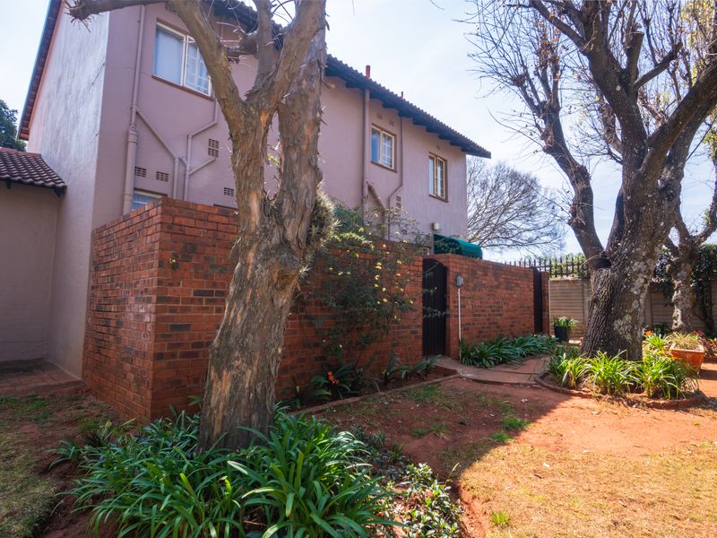 Rear view of the townhouse featuring a brick boundary wall, established trees, and a private garden area.