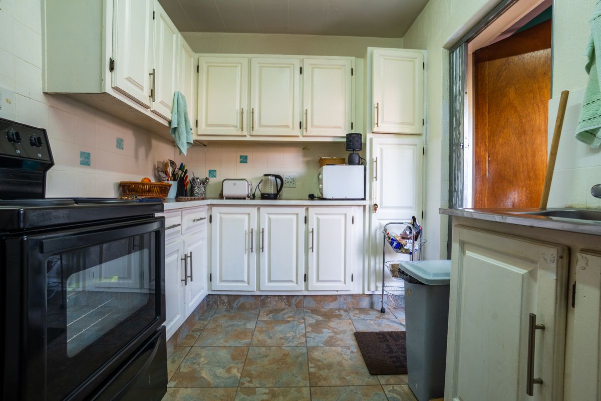 A functional kitchen featuring white built-in cabinetry, a black electric stove, tiled flooring, and a tiled backsplash with direct access to an exterior door.