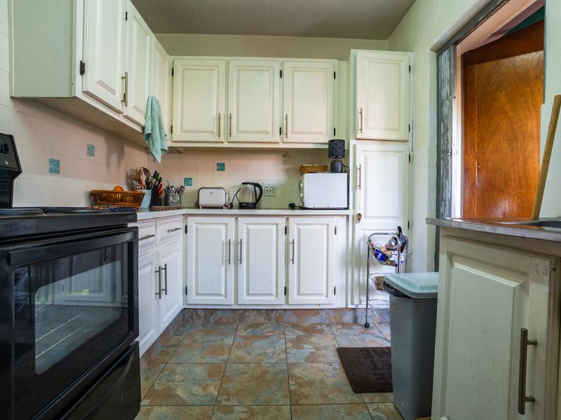 A functional kitchen featuring white built-in cabinetry, a black electric stove, tiled flooring, and a tiled backsplash with direct access to an exterior door.