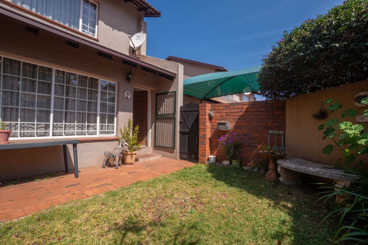 A private rear courtyard featuring brick paving, a small lawn area, a brick boundary wall, and a shaded patio section.