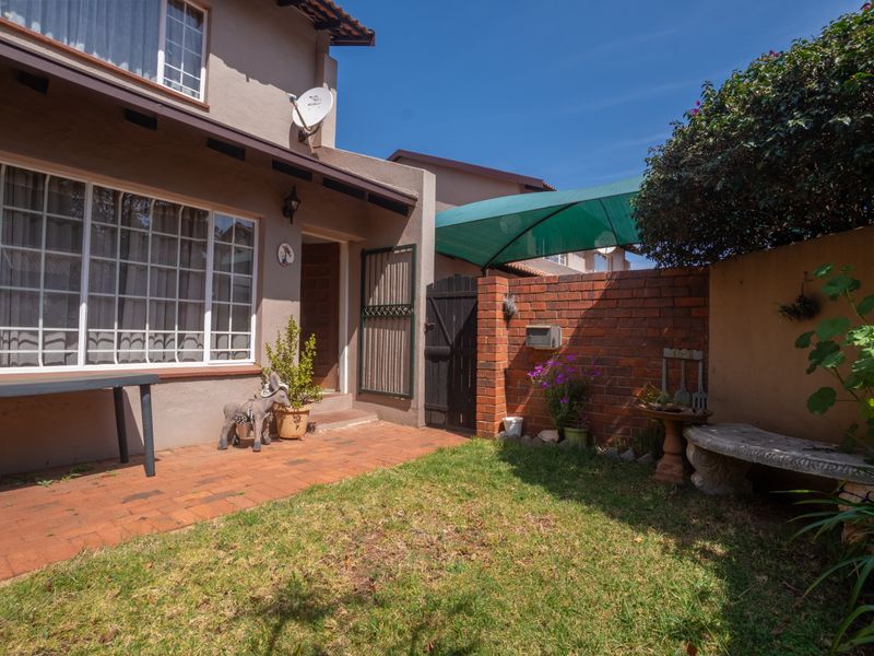 A private rear courtyard featuring brick paving, a small lawn area, a brick boundary wall, and a shaded patio section.
