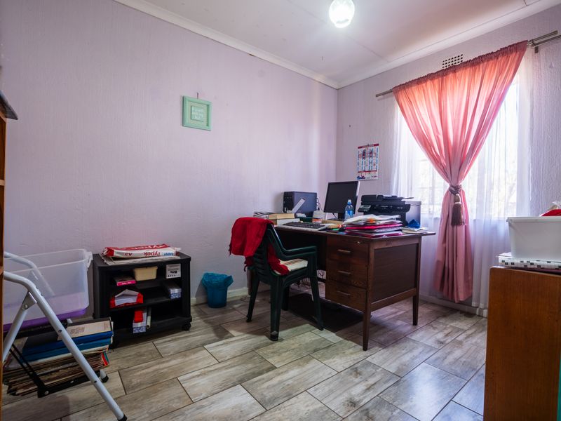 A functional home office space featuring tiled flooring and a window with curtain rails, suitable for a dedicated workspace or study area.