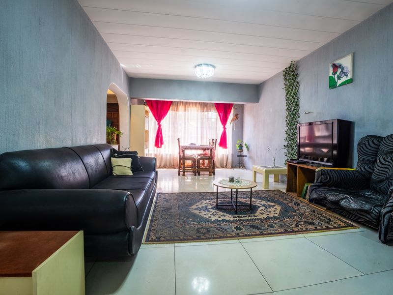 A spacious living room featuring tiled flooring, textured walls, and an archway leading to an adjacent dining area with natural light.