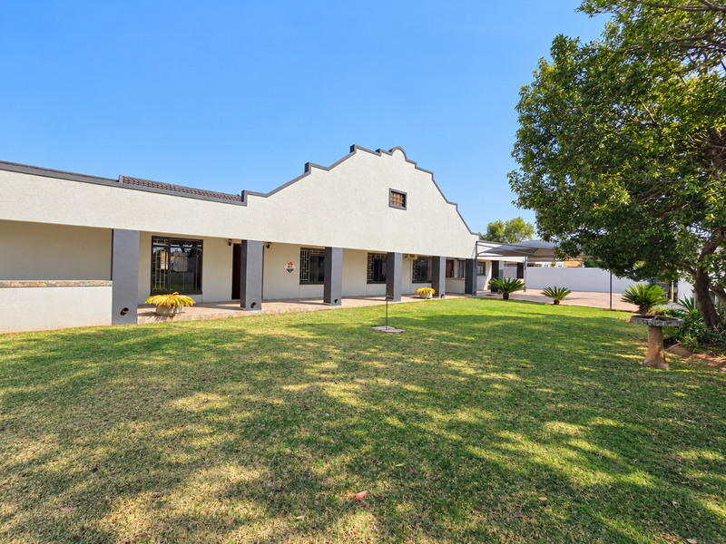 A spacious rear garden featuring a well-maintained lawn and a covered patio area attached to the main house structure.