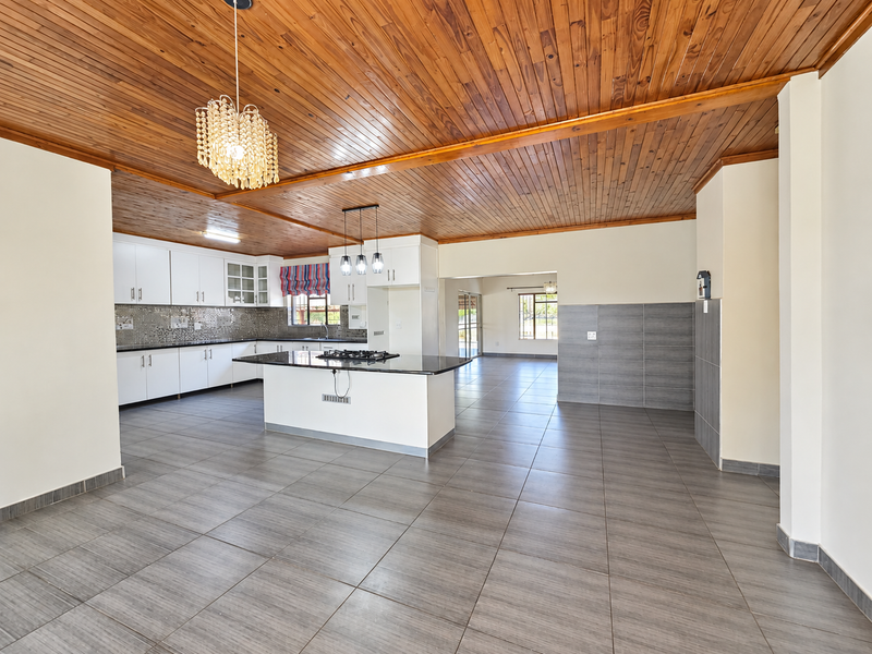 Spacious open-plan kitchen and living area featuring a timber ceiling, modern tiled floors, and a central island with a built-in gas hob.