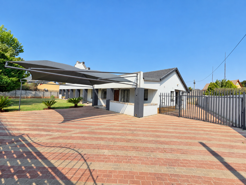 Front exterior view of the property featuring a large paved driveway, shade sail structure, and secure metal perimeter fencing.