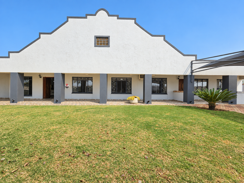 Rear view of a house featuring a distinctive gabled facade, a covered patio area, and a spacious lawn.