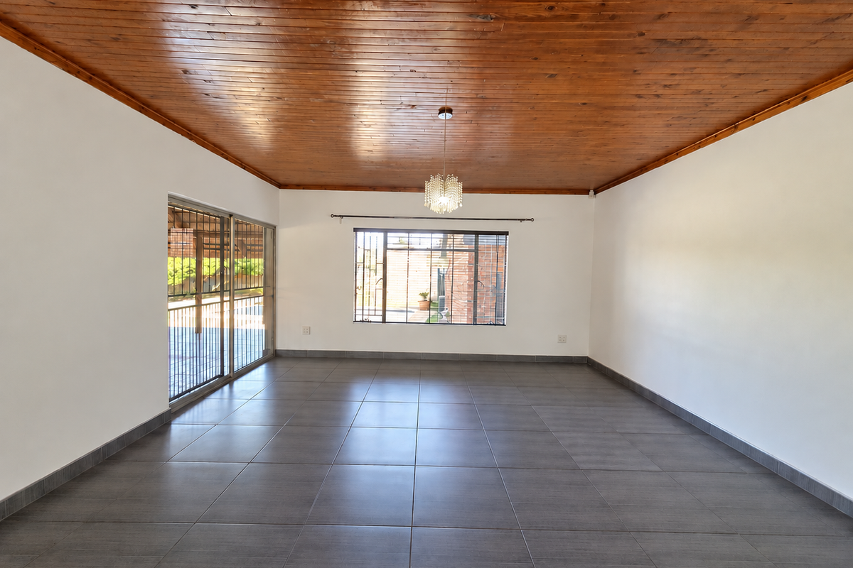 Spacious living area featuring a warm timber tongue and groove ceiling, modern grey ceramic floor tiles, and large windows providing natural light.