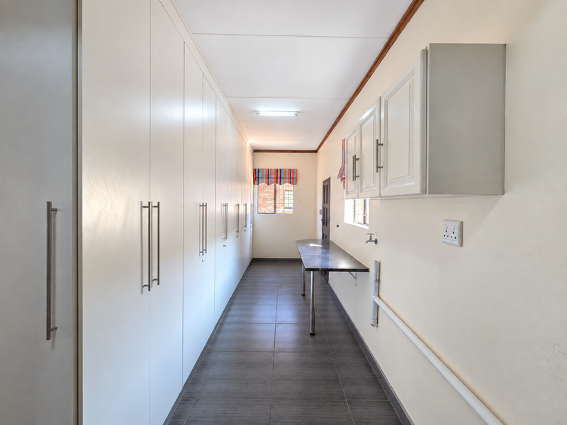 A clean and functional laundry room featuring extensive built-in storage cabinetry, tiled flooring, and a dedicated prep area with plumbing connections.