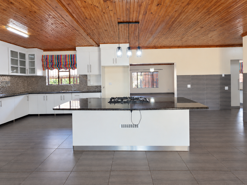 Spacious open-plan kitchen featuring a central island with a gas hob, modern cabinetry, mosaic backsplash, and a warm timber ceiling.