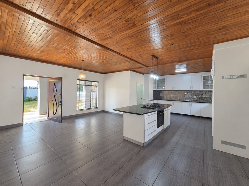Spacious open-plan kitchen and living area featuring a timber ceiling, large kitchen island with gas hob, and modern tiled flooring throughout.