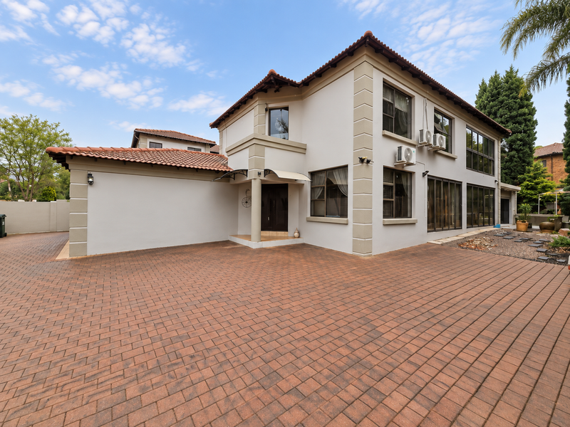 A well-maintained double-storey house featuring a spacious paved driveway, terracotta roof tiles, and modern aluminium window frames with exterior air conditioning units.