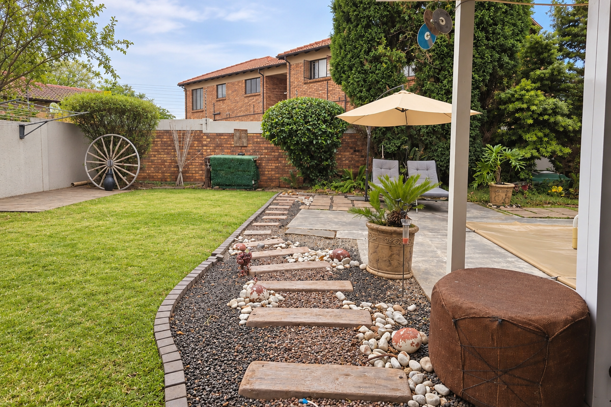 A well-maintained rear garden featuring a paved patio area, lawn, and decorative stone pathway with brick boundary walls.
