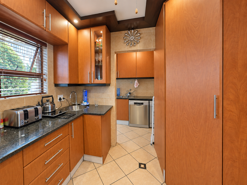 A functional kitchen featuring warm wood-toned cabinetry, granite countertops, tiled backsplash, and a separate scullery area with integrated dishwasher.