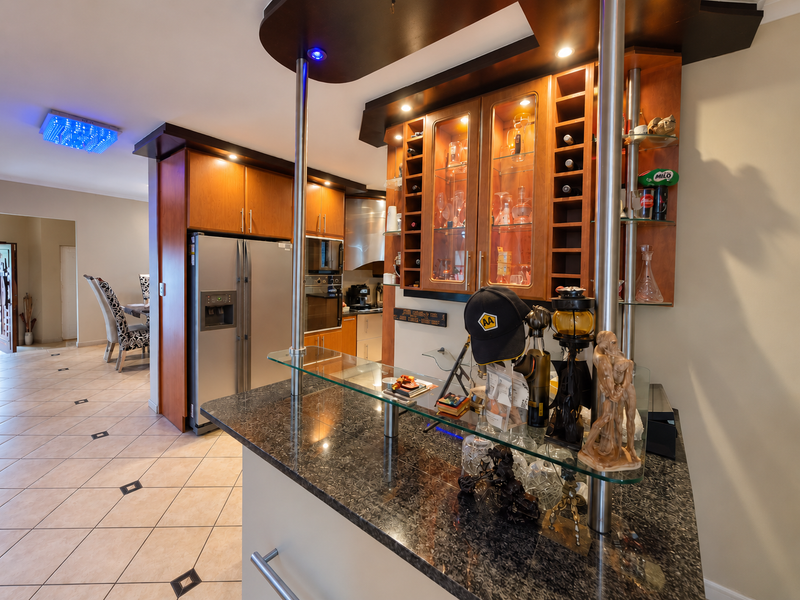 A kitchen featuring dark wood cabinetry, granite countertops, a glass-topped breakfast bar, and integrated stainless steel appliances with tiled flooring.