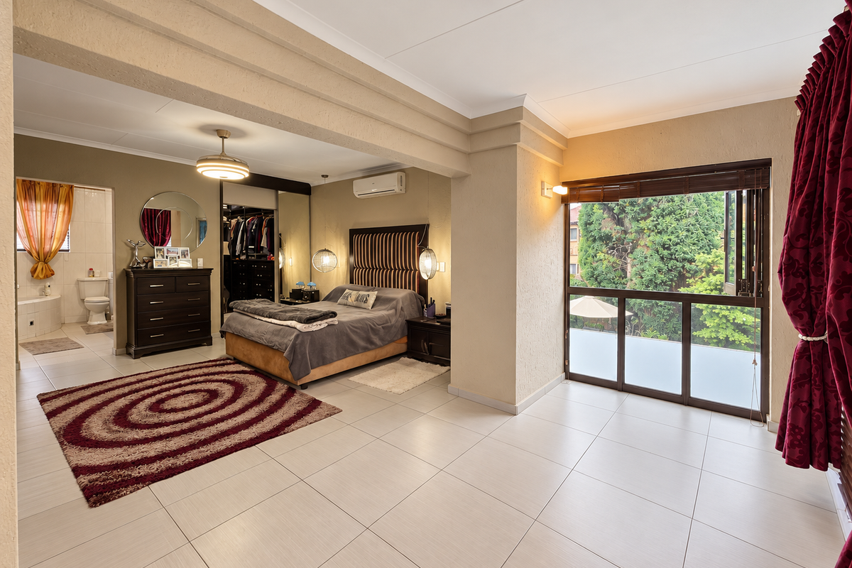 Spacious bedroom featuring tiled flooring, built-in cupboards, an integrated air conditioning unit, and an en-suite bathroom with direct access to an outdoor view.