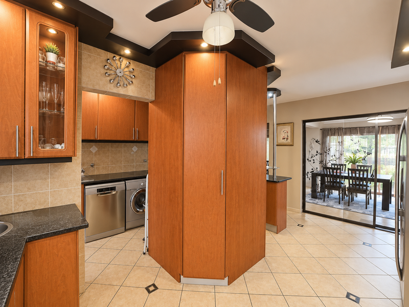 Open plan kitchen and dining area featuring warm wood cabinetry, granite countertops, tiled flooring, and direct access to an outdoor patio through sliding glass doors.