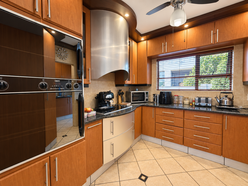 A well-appointed kitchen featuring warm wooden cabinetry, granite countertops, a stainless steel extractor fan, and built-in oven, complemented by tiled flooring.