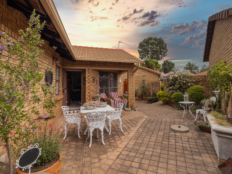 A charming, paved rear patio area featuring facebrick walls, a covered section, and established garden planters, perfect for outdoor relaxation.