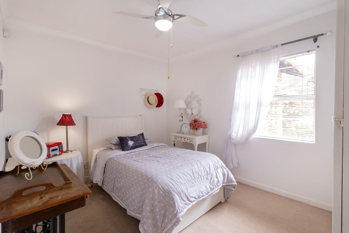 A well-maintained bedroom featuring neutral carpeting, a ceiling fan, and a window with fitted blinds and curtain rod.