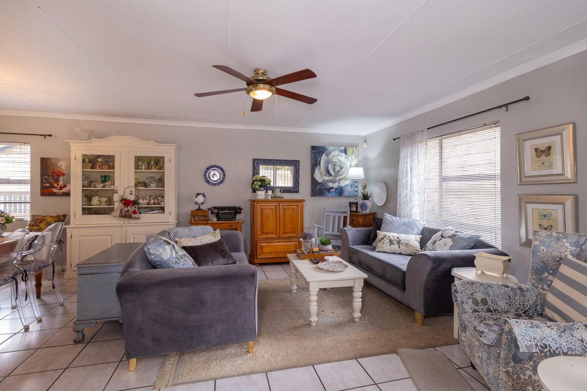 A comfortable living room featuring tiled flooring, a ceiling fan, and large windows with venetian blinds, offering a bright and functional space.