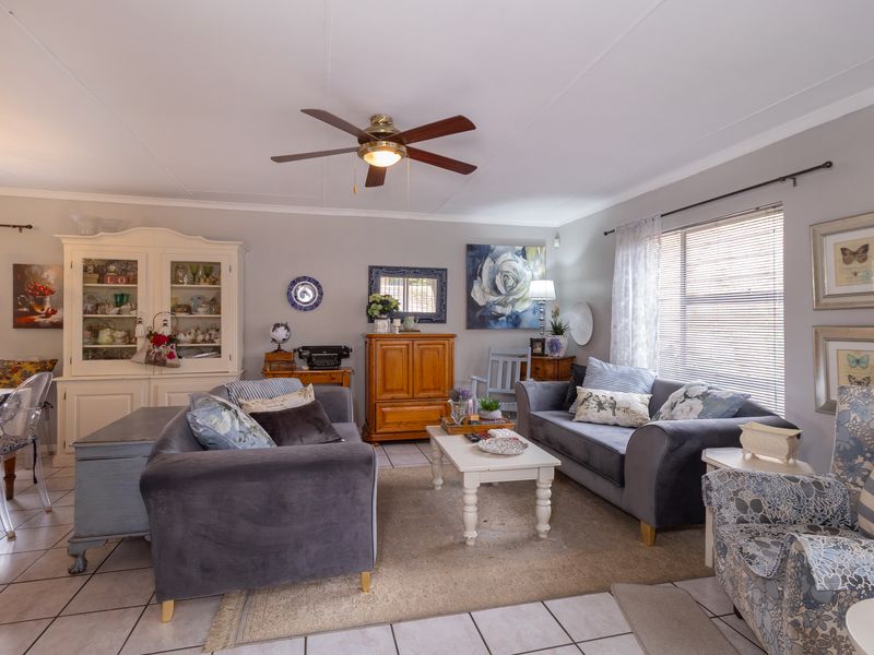 A comfortable living room featuring tiled flooring, a ceiling fan, and large windows with venetian blinds, offering a bright and functional space.