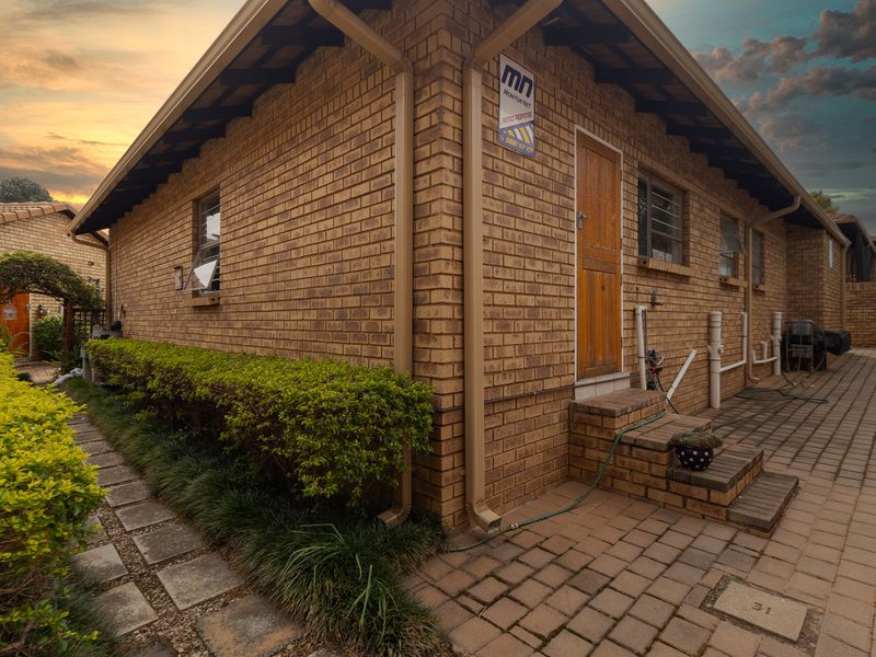 Rear exterior view of a face brick townhouse featuring a paved patio area, timber door, and established garden borders.