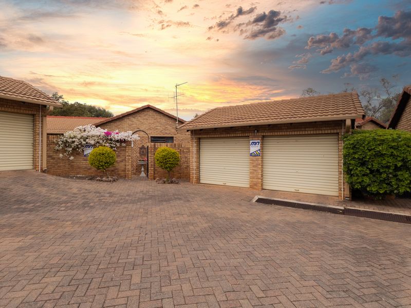 Front exterior view of a townhouse complex featuring brick facades, tiled roofs, and a paved driveway with multiple garage access points.
