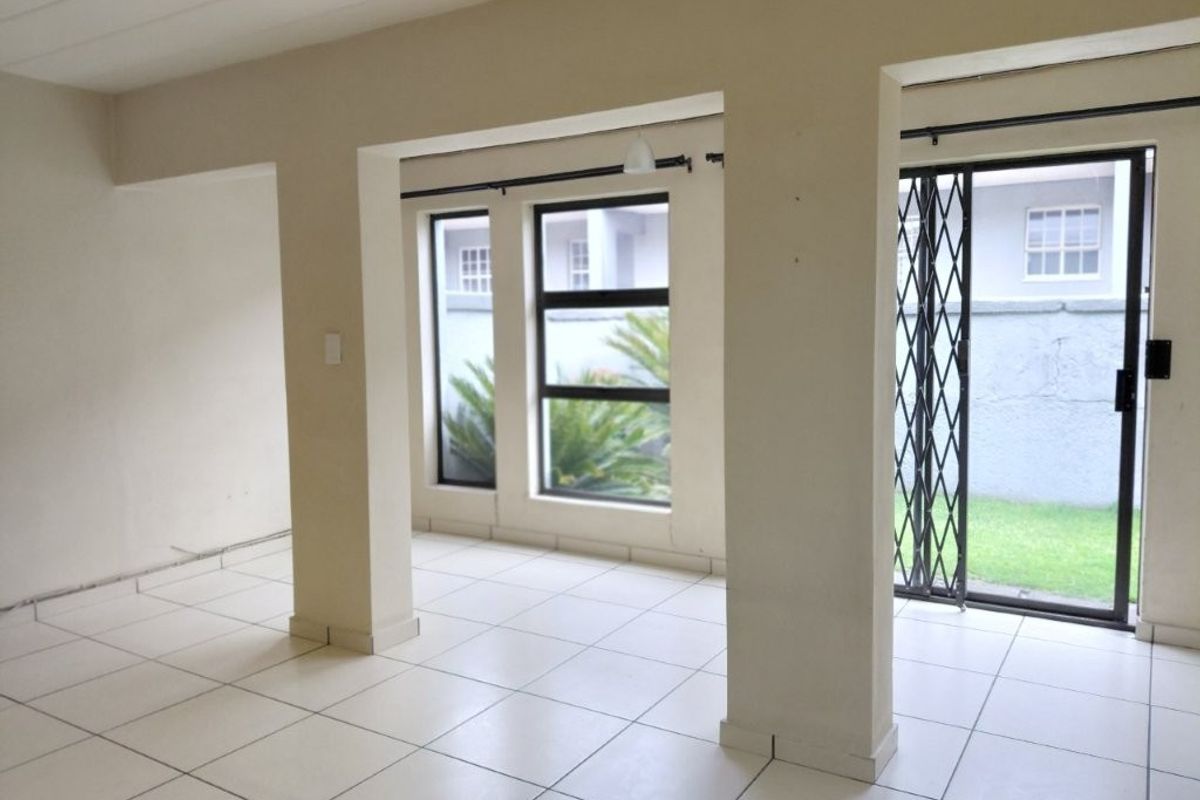 An empty, open-plan living area featuring neutral tiled flooring, large windows, and a sliding door leading to the exterior.