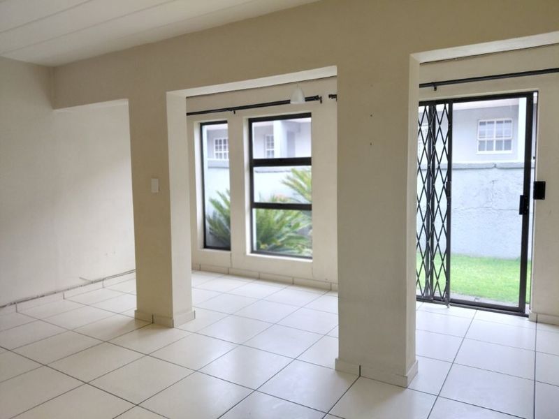 An empty, open-plan living area featuring neutral tiled flooring, large windows, and a sliding door leading to the exterior.