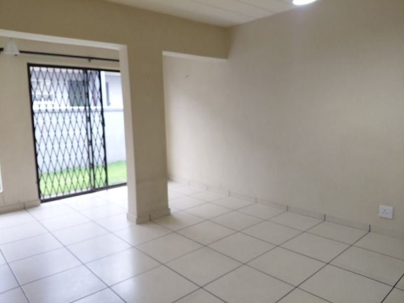 An empty, open-plan living area featuring neutral tiled flooring and a security gate leading to the exterior.